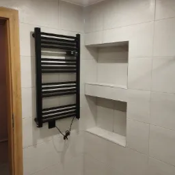 Wykończona łazienka z grzejnikiem drabinkowym w kolorze czarnym i wnękami w ścianie wyłożonej płytkami ceramicznymi w odcieniach bieli i szarości.