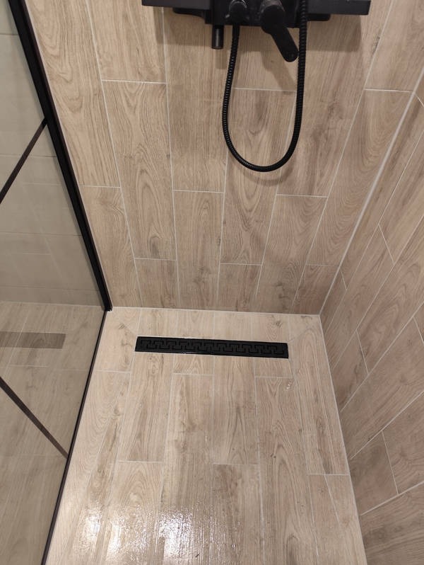 Wykończona kabina prysznicowa z odpływem liniowym i płytkami imitującymi drewno w Makowie Mazowieckim. Czarna armatura i minimalistyczny design.
