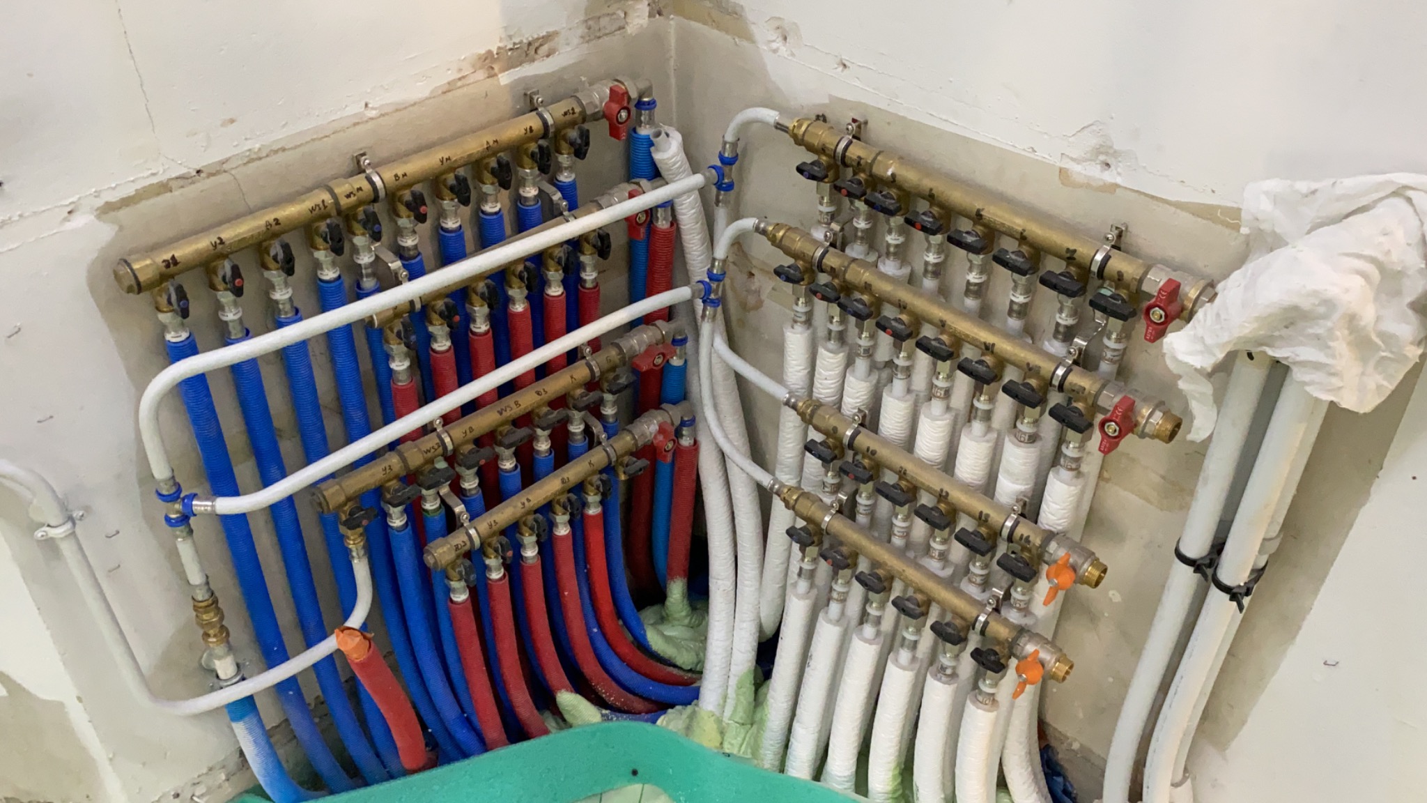 Rozdzielacz instalacji centralnego ogrzewania i wody użytkowej z rurami PEX w kolorach czerwonym, niebieskim i białym, zamontowany na ścianie w rogu pomieszczenia w trakcie remontu.
