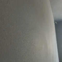 Świeżo nałożony, szary tynk na ścianie wewnętrznej, widoczna faktura oraz fragment sufitu w tle.