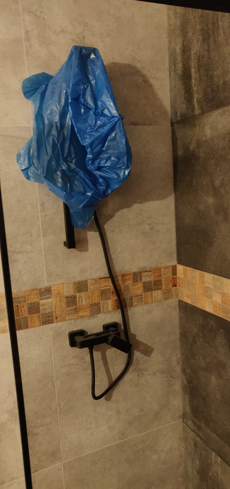 Świeżo wyremontowana łazienka z zamontowaną czarną armaturą, bateria zakryta folią ochronną, widoczne beżowe płytki z dekoracyjnym pasem mozaiki.