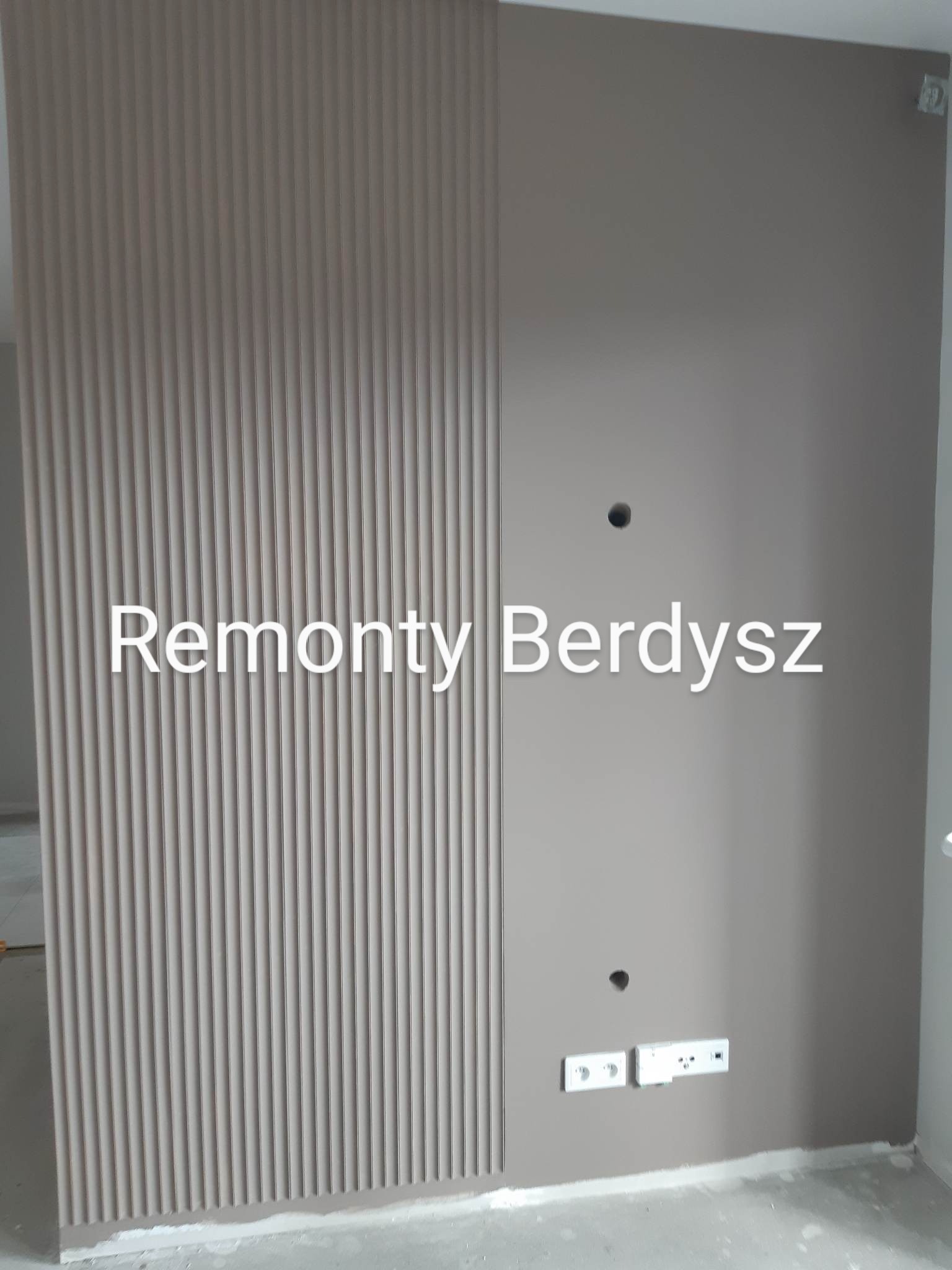 Ściana w odcieniach beżu z dekoracyjnym panelem pionowych listew i gładką powierzchnią, widoczne puszki elektryczne i otwory na kable.