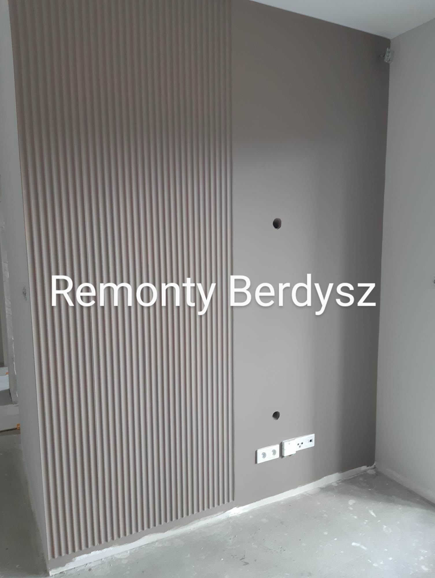 Ściana po remoncie z pionowymi panelami dekoracyjnymi i pomalowaną powierzchnią, widoczne gniazdka elektryczne i otwory na kable, surowy stan podłogi.