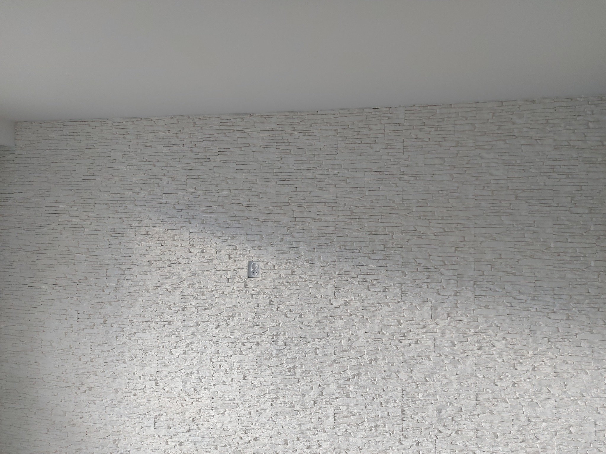 Ściana wewnętrzna wykończona białą okładziną kamienną, widoczne gniazdko elektryczne