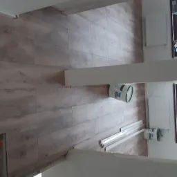 Ułożone panele podłogowe w jasnym odcieniu drewna, widoczny fragment ściany z grzejnikiem, puszka farby i listwy przypodłogowe w folii.