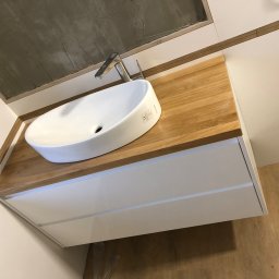 Yomebel-meble na wymiar - Nowoczesna łazienka z owalną umywalką nablatową i drewnianym blatem na białej szafce z szufladami, surowy beton na suficie.