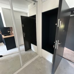 Yomebel-meble na wymiar - Wnętrze z szafą wnękową z lustrzanymi drzwiami przesuwnymi w Stryszawie, odbijające minimalistyczną kuchnię z czarnymi szafkami i drewnianym blatem.