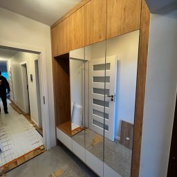 Yomebel-meble na wymiar - Korytarz w trakcie remontu z zamontowaną szafą wnękową z lustrzanymi drzwiami i drewnianymi panelami na górze, widoczne przygotowanie podłogi do położenia paneli.
