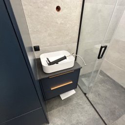 Yomebel-meble na wymiar - Nowoczesna łazienka: ciemnogranatowa szafka pod umywalkę z dwoma szufladami z poziomymi, złotymi uchwytami, biała umywalka nablatowa z czarną baterią, szare płytki na ścianach i podłodze, kabina...