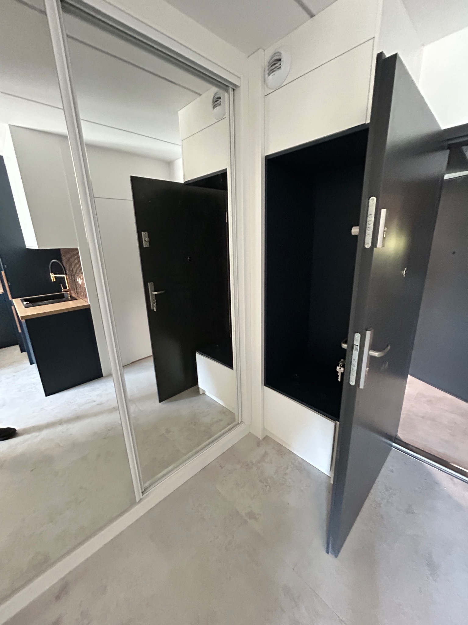 Wnętrze z szafą wnękową z lustrzanymi drzwiami przesuwnymi w Stryszawie, odbijające minimalistyczną kuchnię z czarnymi szafkami i drewnianym blatem.