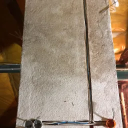 Szara ściana w trakcie prac elektrycznych z widocznymi przewodami w korytkach i puszkach instalacyjnych, izolacja z folii aluminiowej w tle.