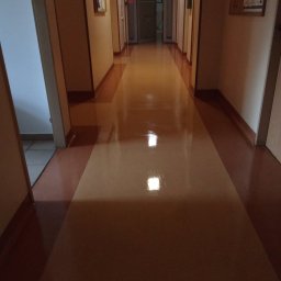 Grupa Oskar White Sp. z o. o. - Błyszcząca, świeżo polimeryzowana podłoga w długim korytarzu biurowym z tablicami ogłoszeń po bokach. Widoczne refleksy świetlne.