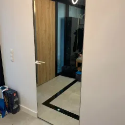 Drzwi szklane z lustrzanym wykończeniem w nowoczesnym wnętrzu, widoczne odbicie drewnianych drzwi i minimalistycznego oświetlenia.