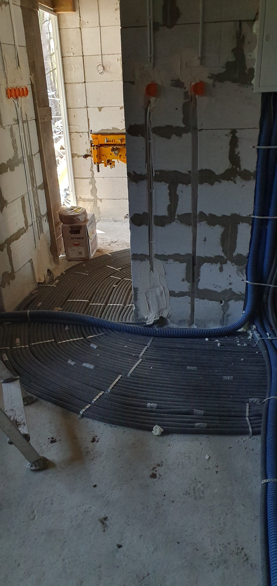 Instalacja ogrzewania podłogowego z rur karbowanych w surowym wnętrzu, widoczne także kable elektryczne w ścianie i skrzynka Bitner.
