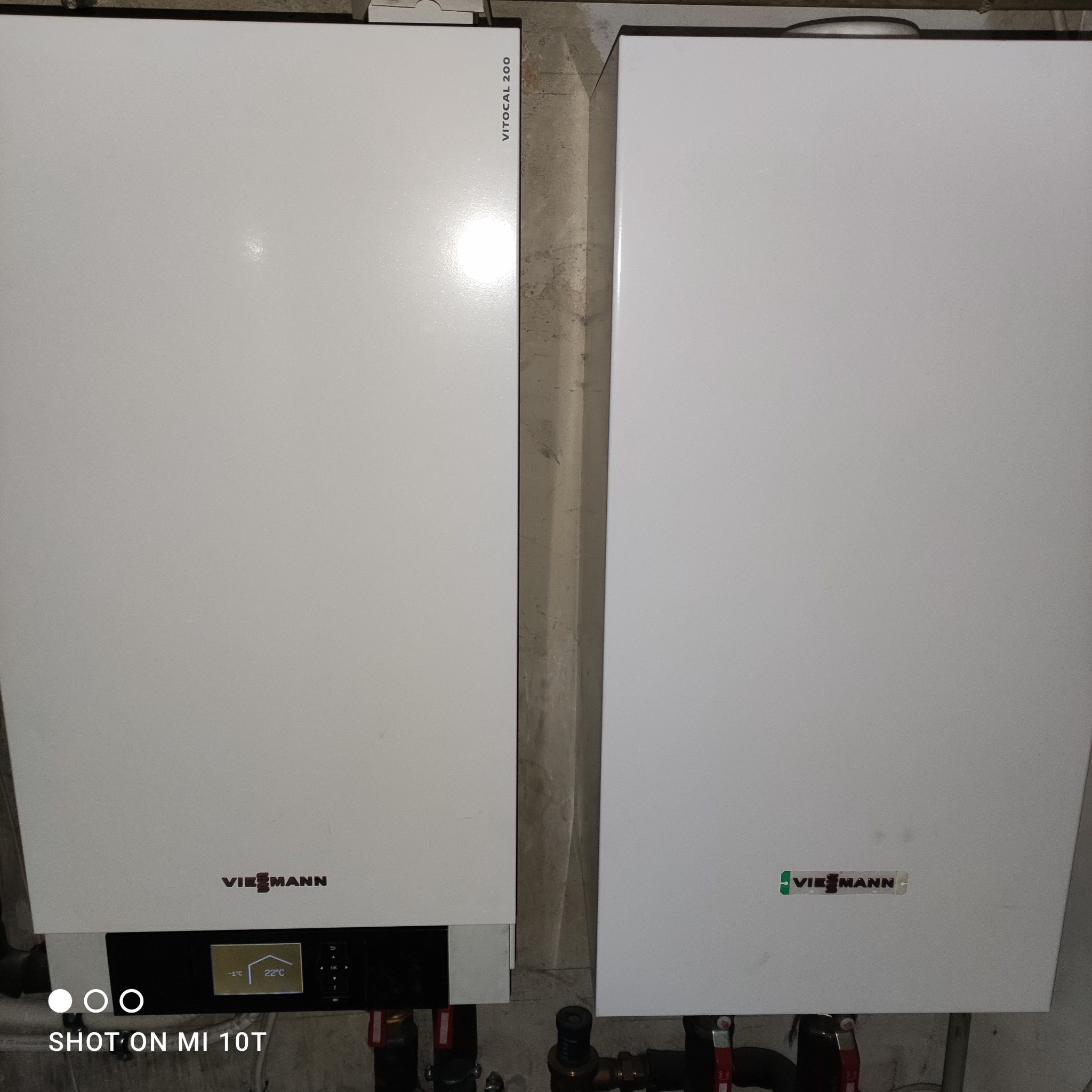 Dwa białe, wiszące urządzenia grzewcze marki Viessmann, model Vitocal 200, z widocznymi przyłączami hydraulicznymi i wyświetlaczami, zamontowane na ścianie w pomieszczeniu technicznym.