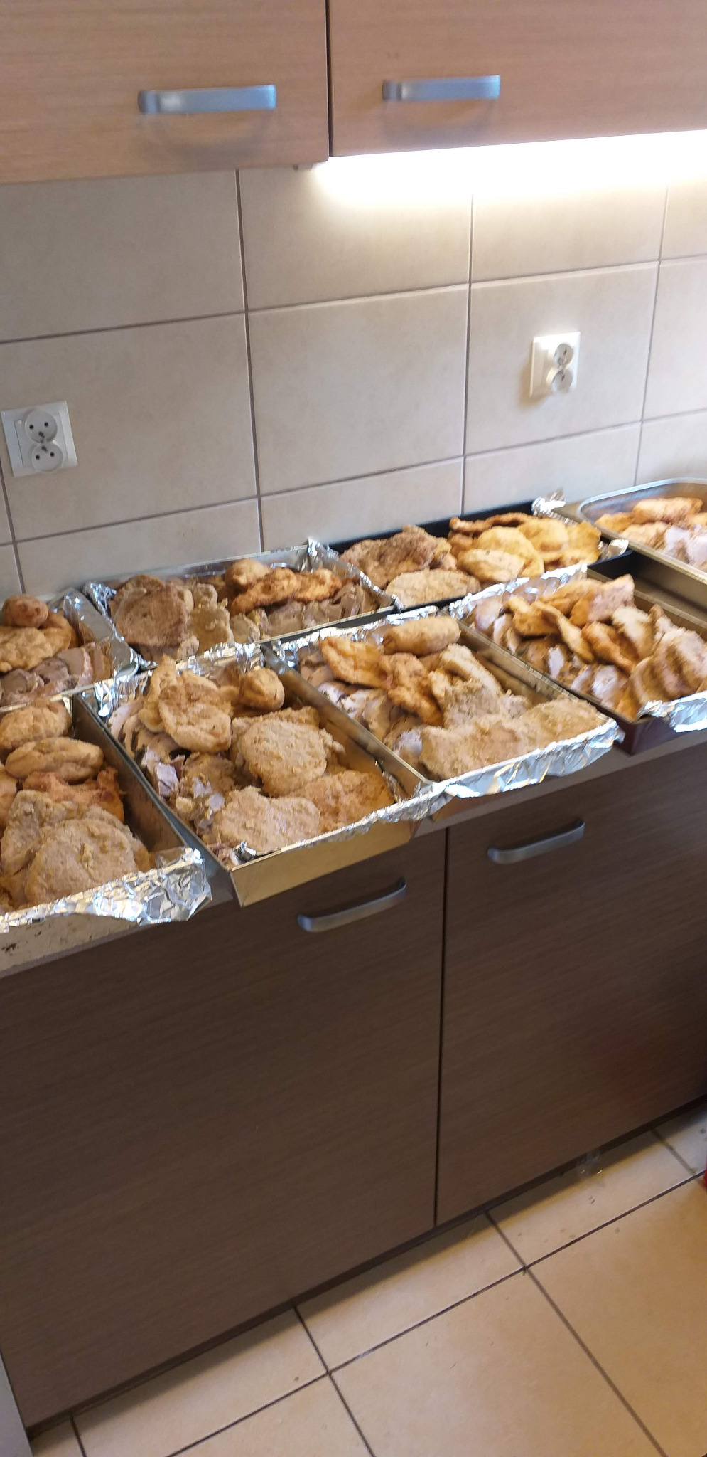 Przygotowane porcje kotletów w panierce ułożone w aluminiowych tackach na blacie kuchennym, gotowe do transportu.