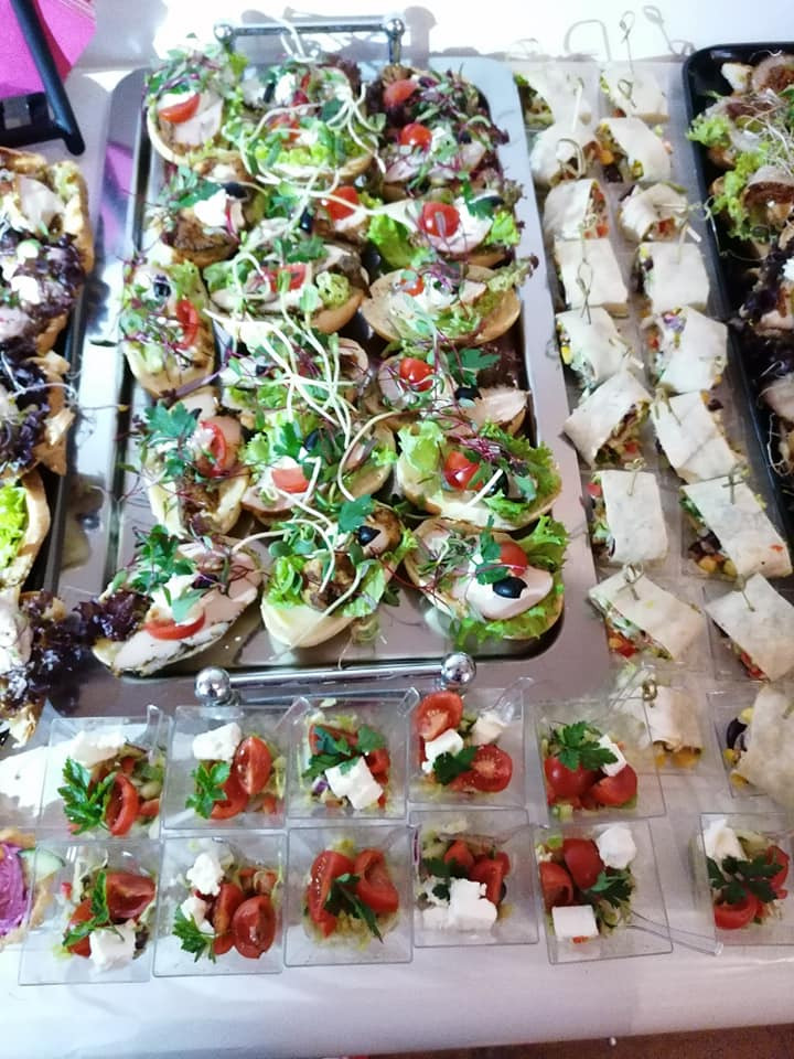 Szwedzki stół z różnorodnymi przekąskami: mini kanapeczki z warzywami i ziołami na srebrnej tacy, roladki tortilli na szpilkach oraz sałatki caprese w przezroczystych pojemniczkach.