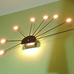 Czarna lampa sufitowa z wieloma ramionami zakończonymi okrągłymi, ciepłymi żarówkami, zamontowana na zielonej ścianie, rzucająca wyraźny cień.