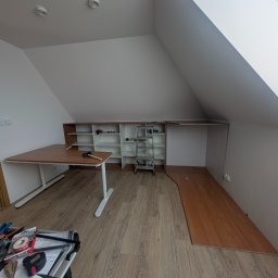 Przedsiębiorstwo Usługowe MAX Wojciech Daniluk - Montaż mebli na poddaszu: biurko z młotkiem, regał z drabiną, fragment ułożonej podłogi. Widoczne narzędzia i akcesoria montażowe.
