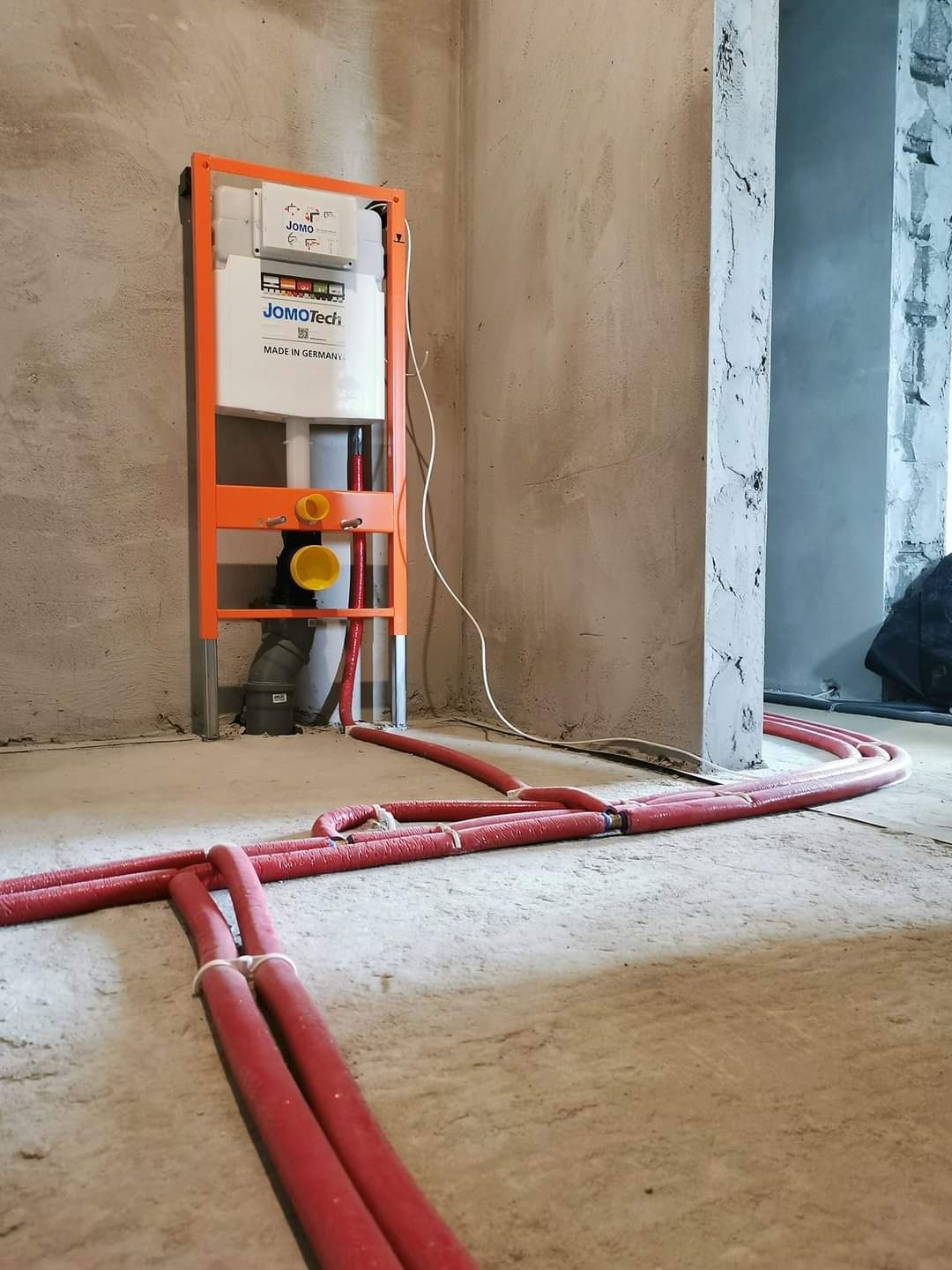 Instalacja podtynkowa JOMO Tech z czerwonymi rurami grzewczymi na podłodze w surowym stanie w Żyznowie, widok z dołu.