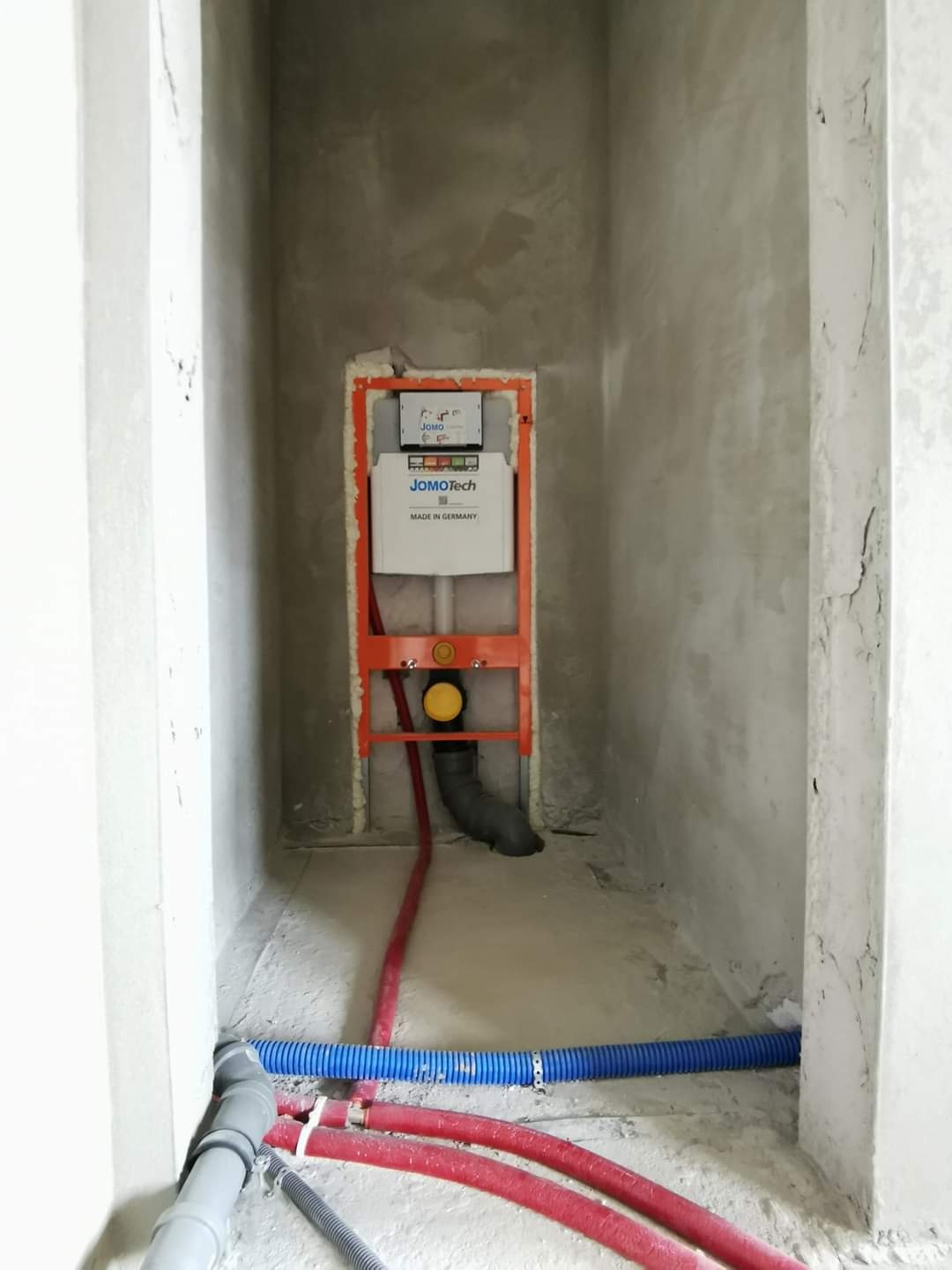 Montaż podtynkowego stelaża WC JOMOTech z widocznymi rurami dopływowymi i odpływowymi w surowym pomieszczeniu łazienki przed wykończeniem.