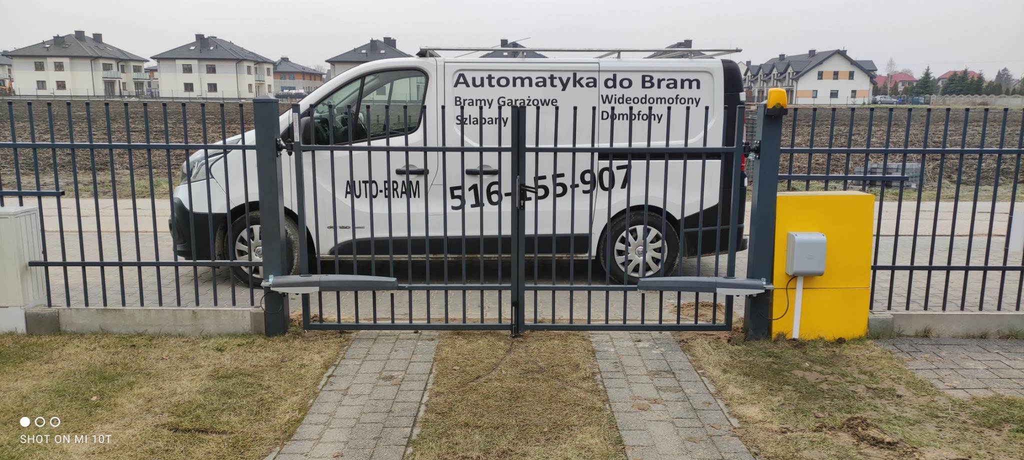 Szara brama wjazdowa z automatyką, widoczny siłownik Came AXL i skrzynka sterująca, na tle biały samochód dostawczy z reklamą firmy.
