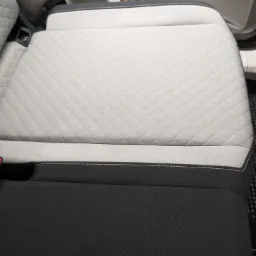 Szara, pikowana tapicerka tylnego siedzenia samochodu z widocznym pasem bezpieczeństwa i elementami wnętrza pojazdu.