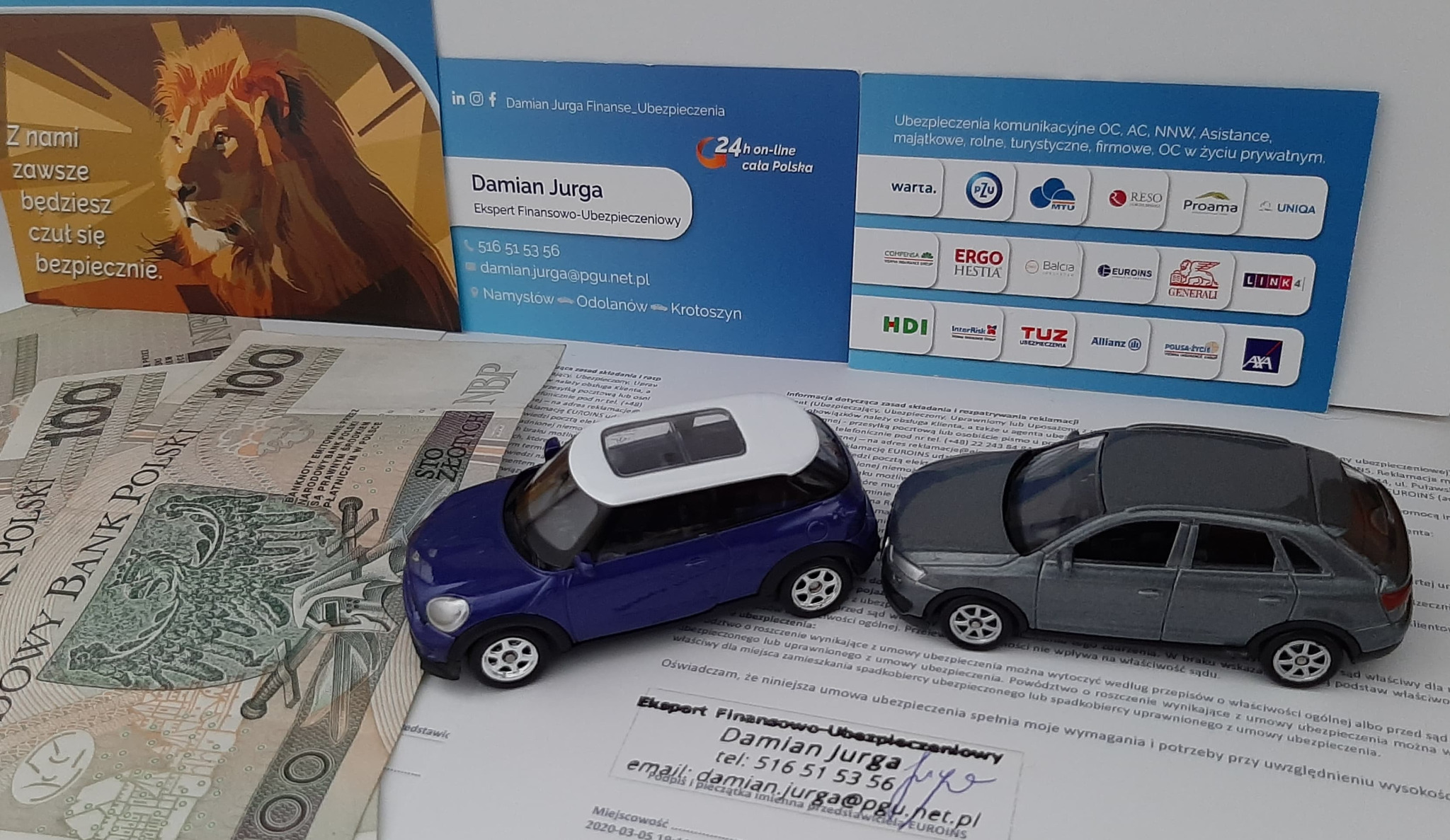 Dwa modele samochodów, niebieski i szary, leżące na dokumencie obok banknotów 100 zł, z wizytówką eksperta finansowo-ubezpieczeniowego i logo firm ubezpieczeniowych w tle.