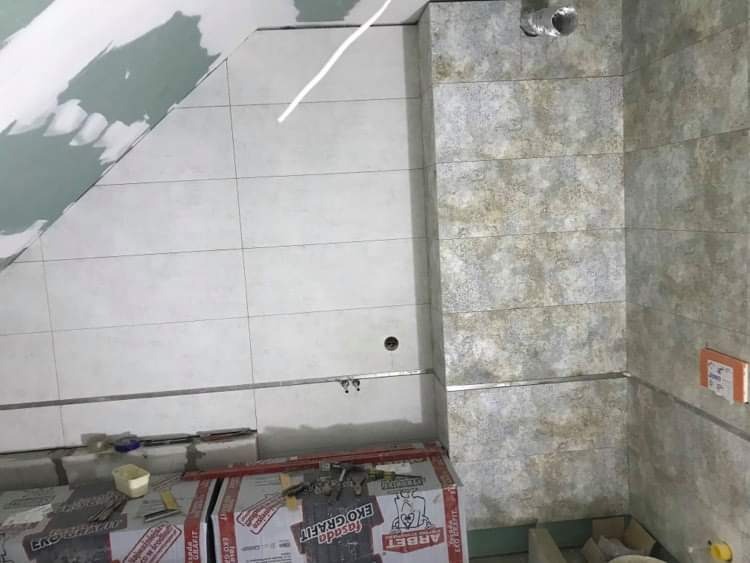 Układanie płytek w łazience na poddaszu, widoczne kartony z klejem do płytek Fasada Eko Grafit, metalowe listwy wykończeniowe i fragment instalacji wentylacyjnej.