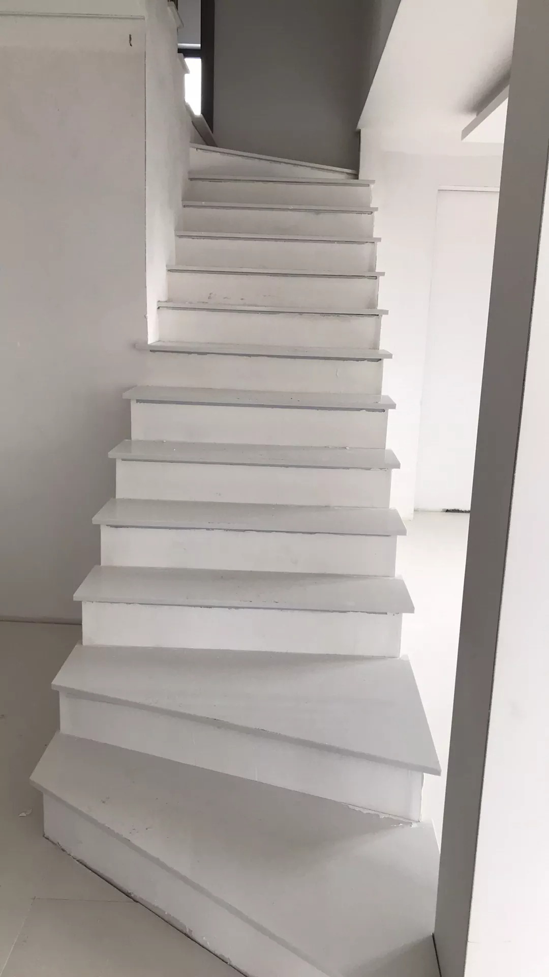Białe, drewniane schody w jasnym wnętrzu, świeżo pomalowane, widoczne niedoskonałości wykończenia.