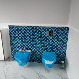 VP Remont Volodymyr Yavorskyi - Bidet i toaleta w trakcie zabezpieczania folią ochronną, przed położeniem płytek o wzorze rybiej łuski w odcieniach niebieskiego i zielonego, na podłodze płytki imitujące marmur, widoczny środek...