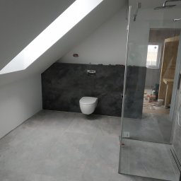 VP Remont Volodymyr Yavorskyi - Nowoczesna łazienka na poddaszu z szarą płytką podłogową, ścianą w ciemnym tynku dekoracyjnym, kabiną prysznicową ze szkła i wiszącą toaletą. Widoczne narzędzia i materiały budowlane w tle.