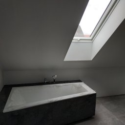 VP Remont Volodymyr Yavorskyi - Wanna obudowana ciemnymi płytkami w łazience na poddaszu, zabezpieczona folią ochronną, widoczne okno dachowe.