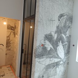 VP Remont Volodymyr Yavorskyi - Ściana z szarą tapetą w motywy kwiatowe i czarna, przeszklona rama drzwi w trakcie prac wykończeniowych, widoczne kable i zabezpieczenia podłogi.