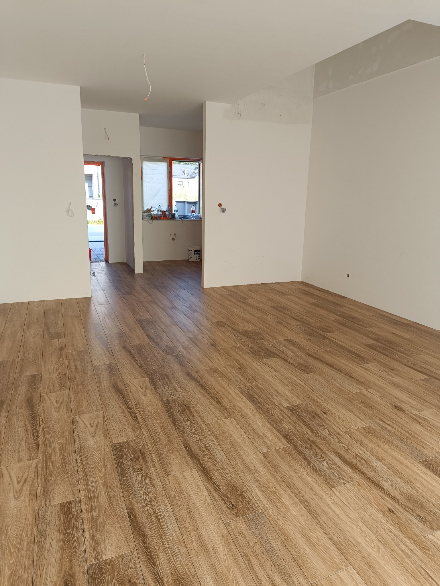 Wykończone wnętrze mieszkania z drewnopodobną podłogą ułożoną w jodełkę, widoczne białe ściany w trakcie malowania i przygotowania do wykończenia.