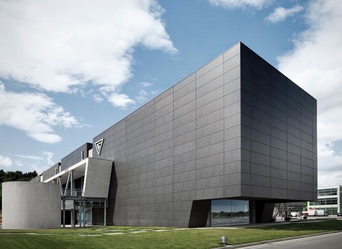 Nowoczesny budynek biurowy z elewacją z szarych płyt kamiennych, widoczny z perspektywy trawnika, z logo firmy na elewacji. Płyty elewacyjne ułożone w regularny wzór z delikatnymi fugami.