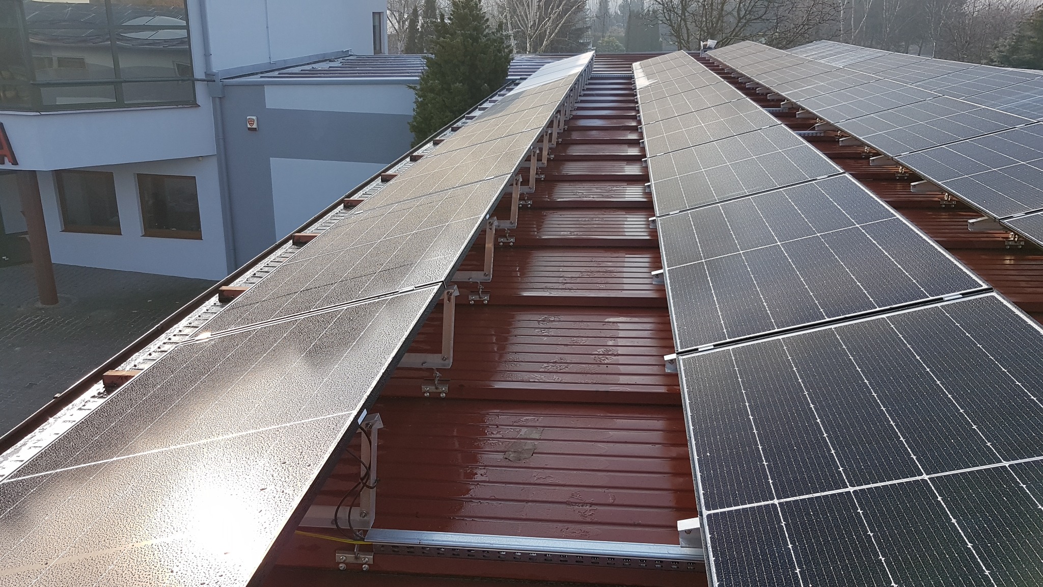 Rzędy paneli słonecznych pokrytych kroplami wody zamontowane na metalowym dachu budynku, widok z góry pod kątem.