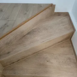 Schody wyłożone płytkami ceramicznymi imitującymi drewno, z drewnianą listwą na krawędzi stopnia, widok z góry.