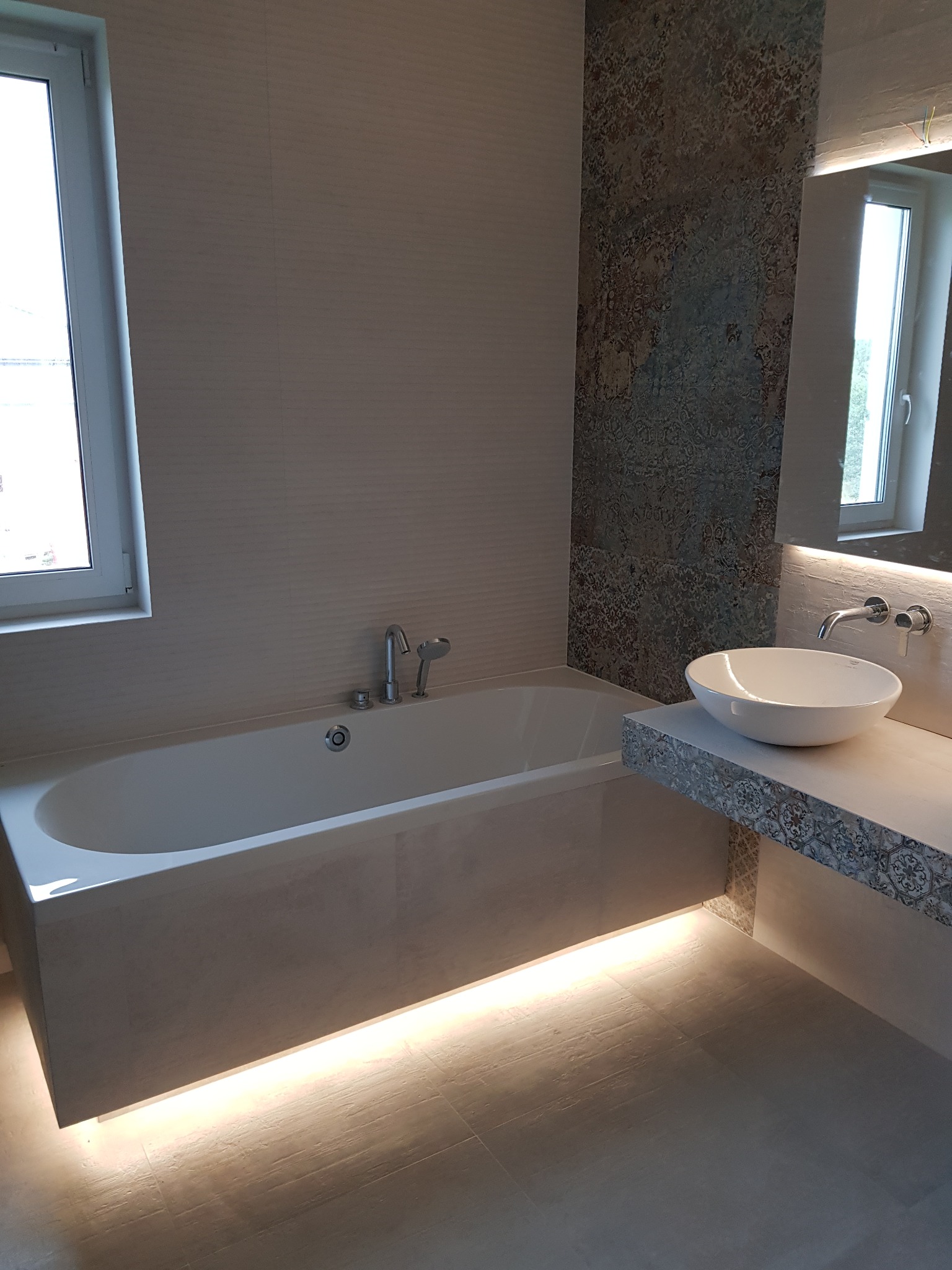 Nowoczesna łazienka z podświetlaną wanną, umywalką nablatową i dekoracyjną ścianą z wzorzystymi płytkami.