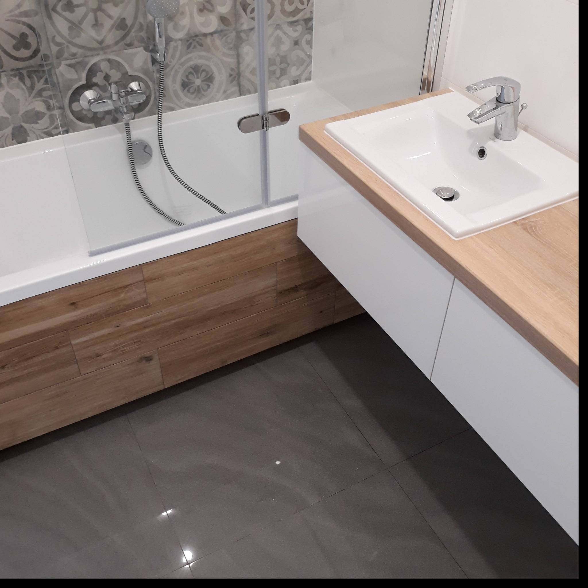 Nowoczesna łazienka po remoncie: wanna z parawanem, umywalka nablatowa z drewnianym blatem i szara podłoga z płytek.