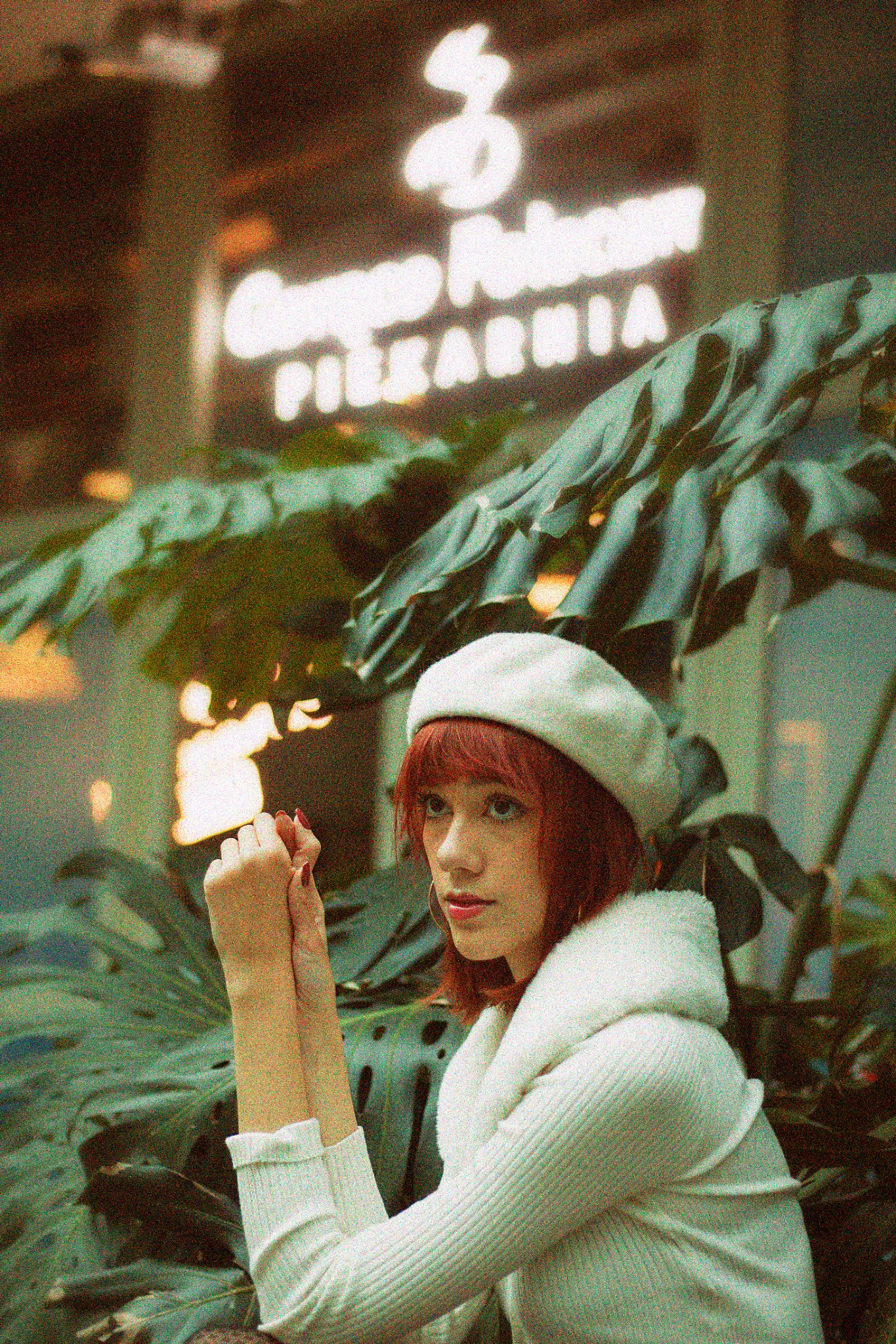 Portret kobiety w białym berecie i swetrze na tle tropikalnych roślin i neonu 'Congee Palace PIEKARNIA'