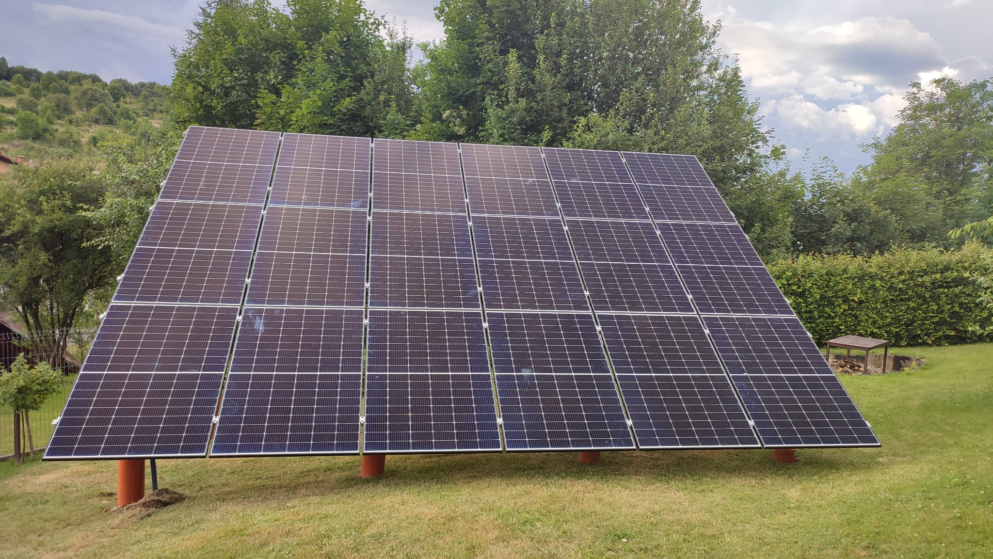 Instalacja paneli słonecznych w Porąbce na trawiastym terenie, widoczne podpory w kolorze ceglastym i tło z drzewami.