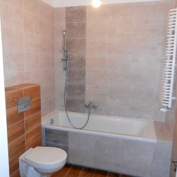 M&L Group Igor Leszczyński - Wykończona łazienka z beżowymi i szarymi płytkami, drewnopodobną zabudową toalety i grzejnikiem drabinkowym.