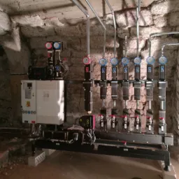 Instalacja grzewcza z manometrami i pompą Grundfos X w piwnicy o kamiennych ścianach.