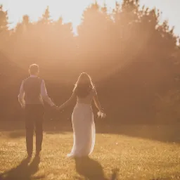 Para młoda idzie przez pole w promieniach zachodzącego słońca, ona trzyma buty w ręku, widok z tyłu.