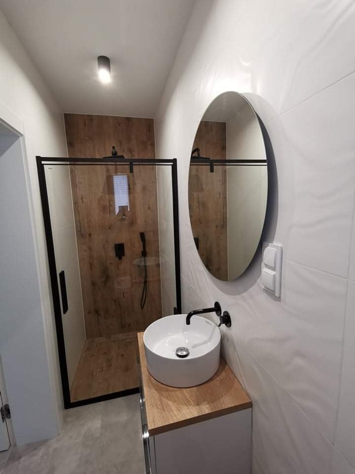 Nowoczesna łazienka z kabiną prysznicową typu walk-in z czarnymi ramami, okrągłym lustrem, umywalką nablatową i armaturą w kolorze czarnym mat.