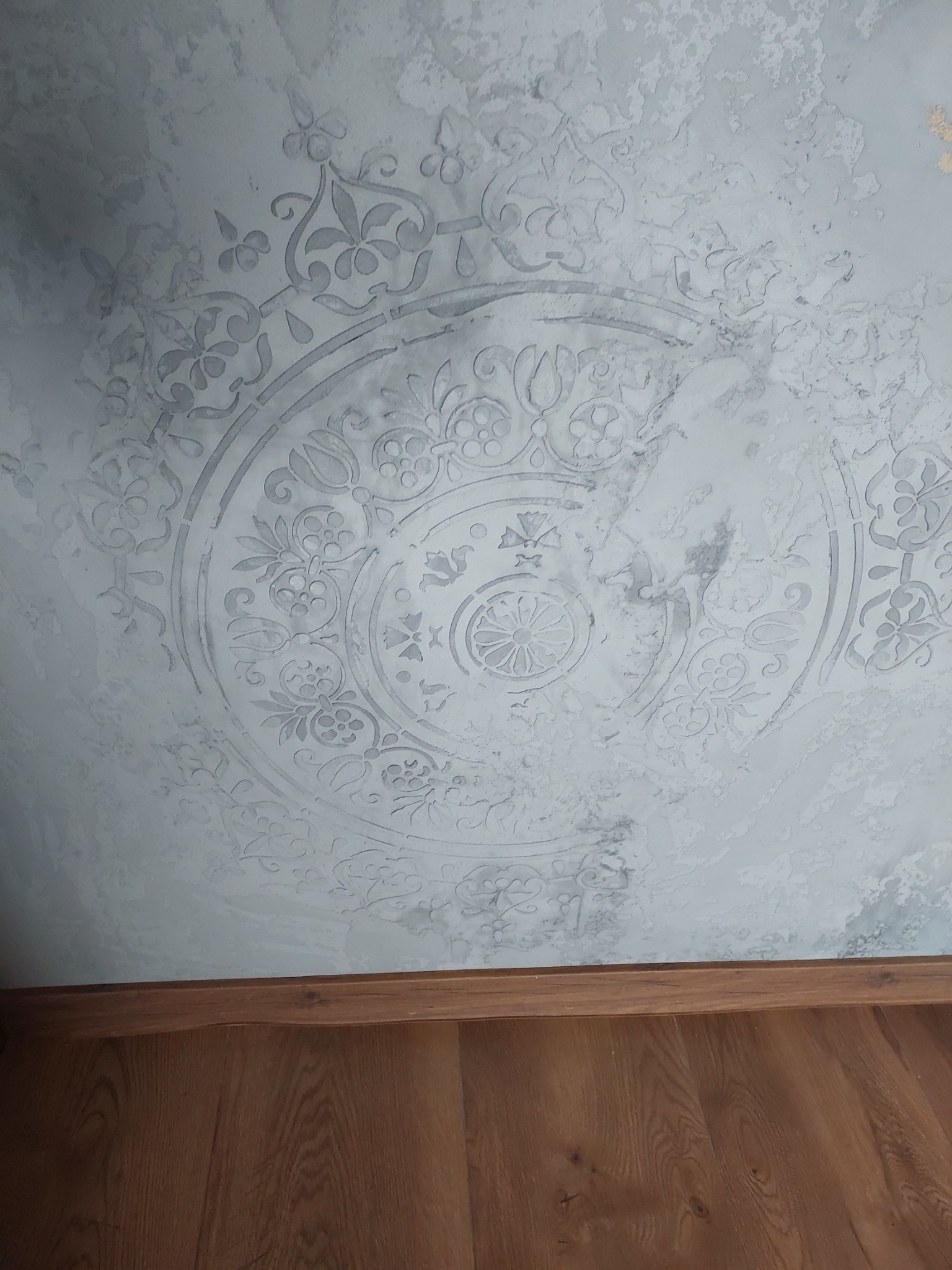 Dekoracyjna ściana z szarymi wzorami w kształcie koła i kwiatów, dolna część ściany z drewnianą listwą przypodłogową.