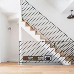 Minimalistyczne schody z drewnianymi stopniami i czarną, ukośną balustradą z metalowych prętów. Na dolnym poziomie balustrady umieszczone tablice rejestracyjne i czarno-biała fotografia.