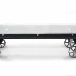 Stolik kawowy na kółkach w stylu industrialnym, z blatem ze szkła i metalową konstrukcją przypominającą fragment torowiska, widoczne nity i mocowania.