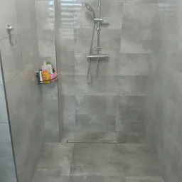 Wykończona kabina prysznicowa z szarymi, matowymi płytkami, odpływem liniowym i półką z kosmetykami.